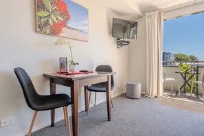 A room with a desk, two chairs, a TV, a balcony with a table and chairs, and a trash bin. - Chelsea Park Motor Lodge Nelson (Nelson)