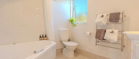 Een badkamer met een bad, toilet en een raam met een plant.