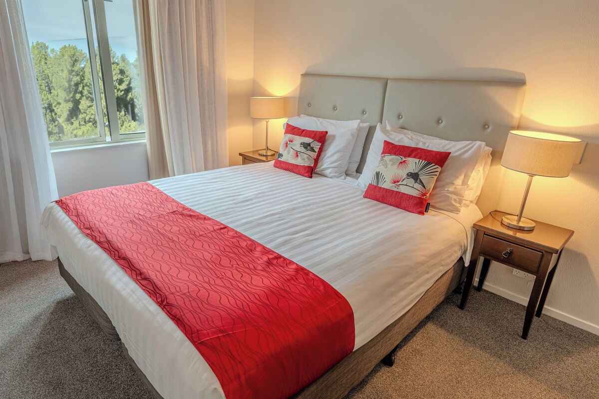 A bed with a red and white bedspread, two bedside lamps, and a nightstand with a lamp.