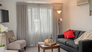 Uma sala de estar com sofá, poltrona, mesa de centro, abajur e televisão.