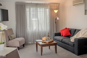A living room with a sofa, a chair, a coffee table, a lamp, and a TV.