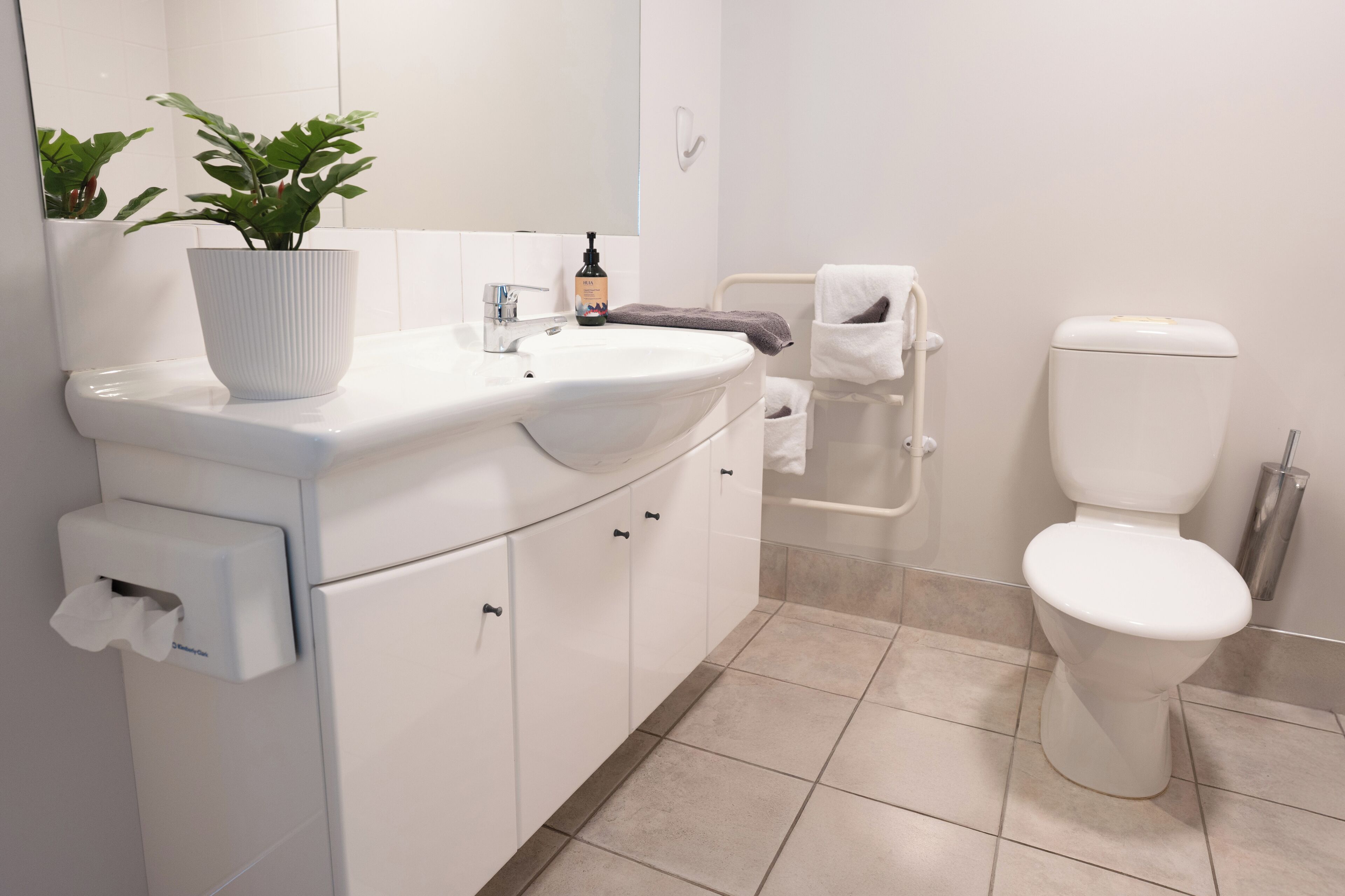 Baño con lavamanos blanco, espejo, inodoro y una planta en maceta.