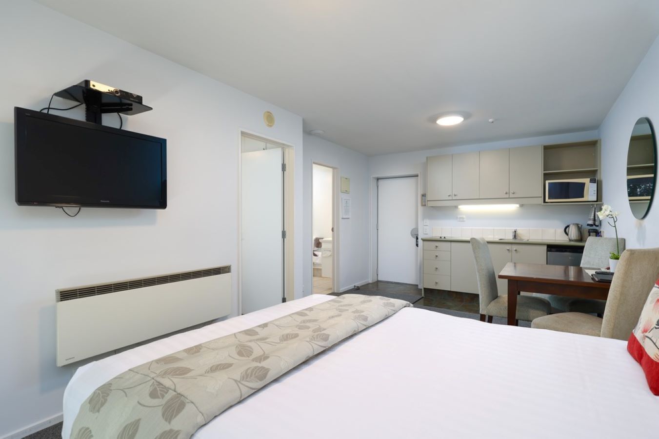 Ein Hotelzimmer mit Bett, Wandfernseher, einer Küchenzeile und einem durchgegangene Tür sichtbaren Badezimmer.