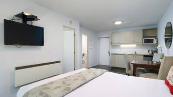 Een hotelkamer met een bed, een aan de muur bevestigde televisie, een kitchenette en een badkamer zichtbaar door een geopende deur.