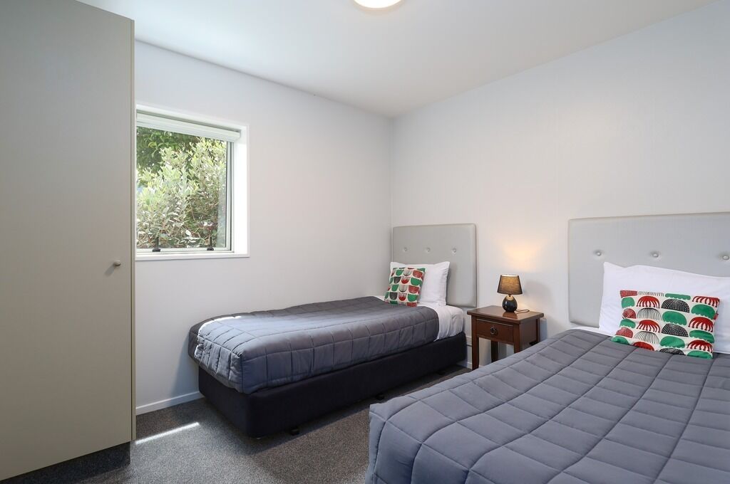 Un dormitorio con dos camas, una ventana y una mesita de noche con lámpara.