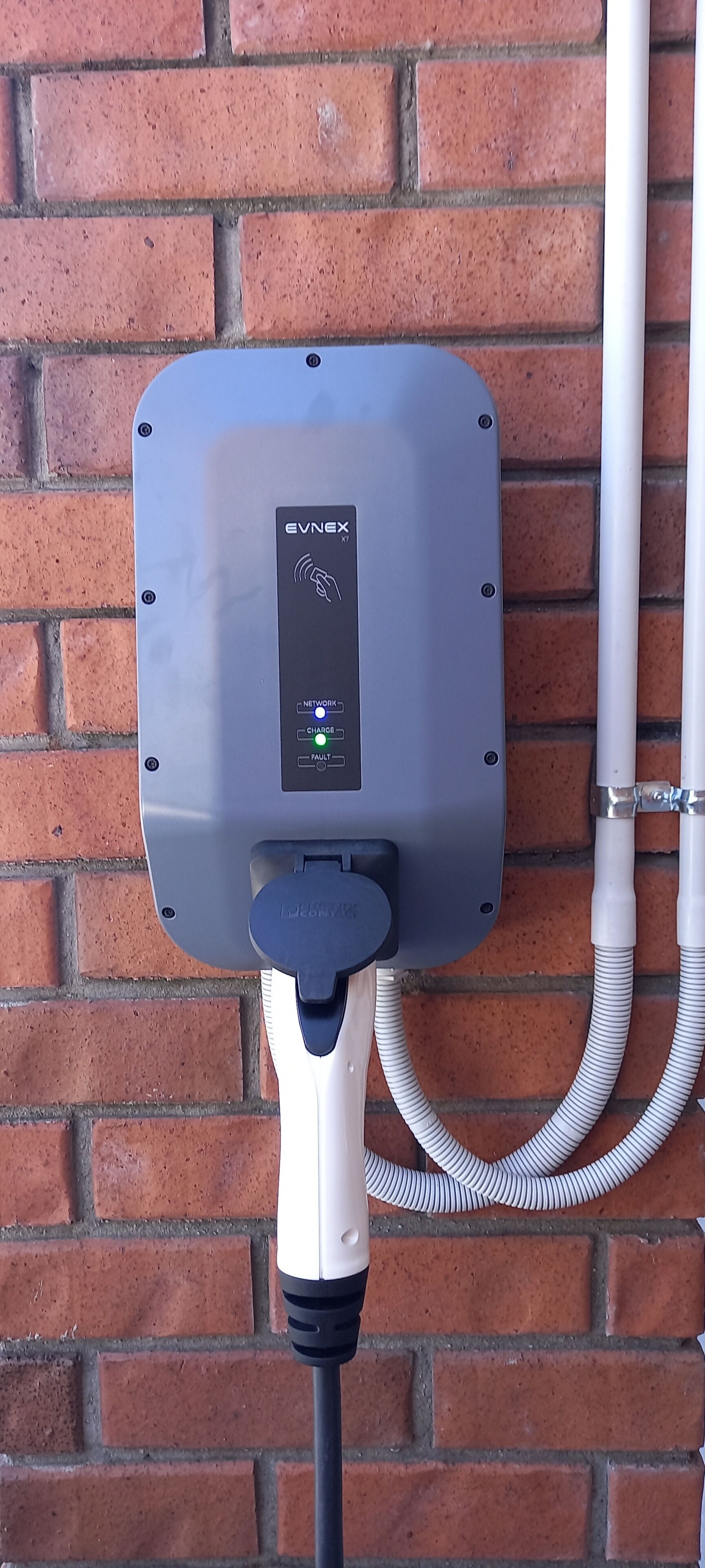 An EVNEX charging station mounted on a brick wall with a white cable connected to it.