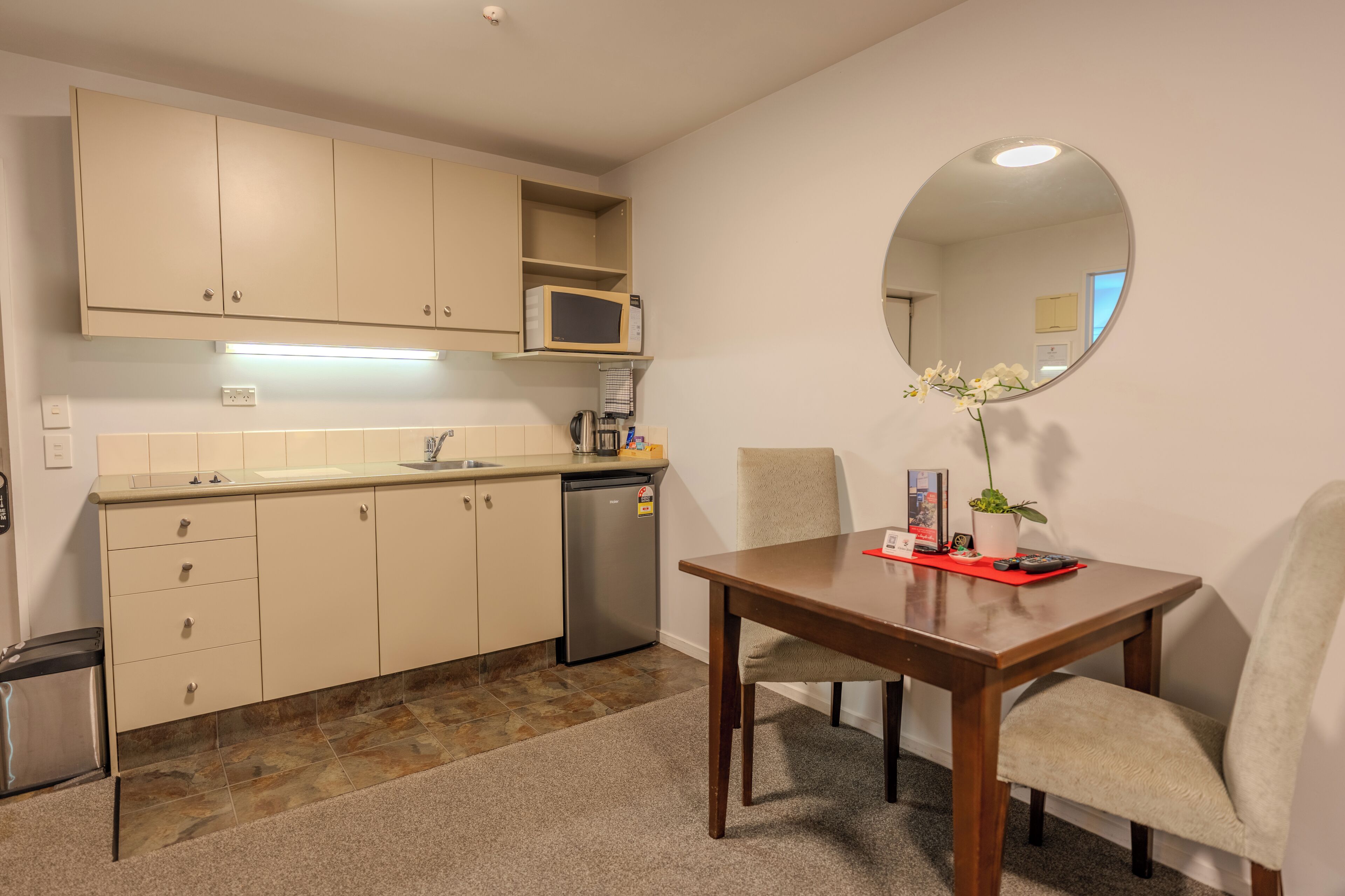 Une cuisine compacte équipée d’un four à micro-ondes, d’un évier et d’un lave-vaisselle. On y trouve une table à manger avec des chaises, ainsi qu’un miroir au mur.