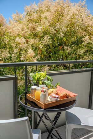 Un balcón con una mesa lista para el desayuno, incluyendo croissants, una botella y una bandeja con una bebida.