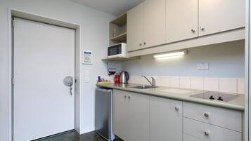 A compact kitchen with white cabinets, a stainless steel sink, and a microwave.