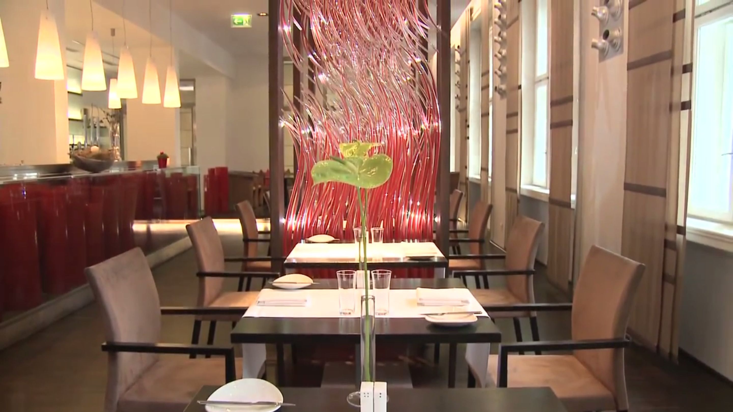 A restaurant with a long table, chairs, and a decorative plant in the center.
