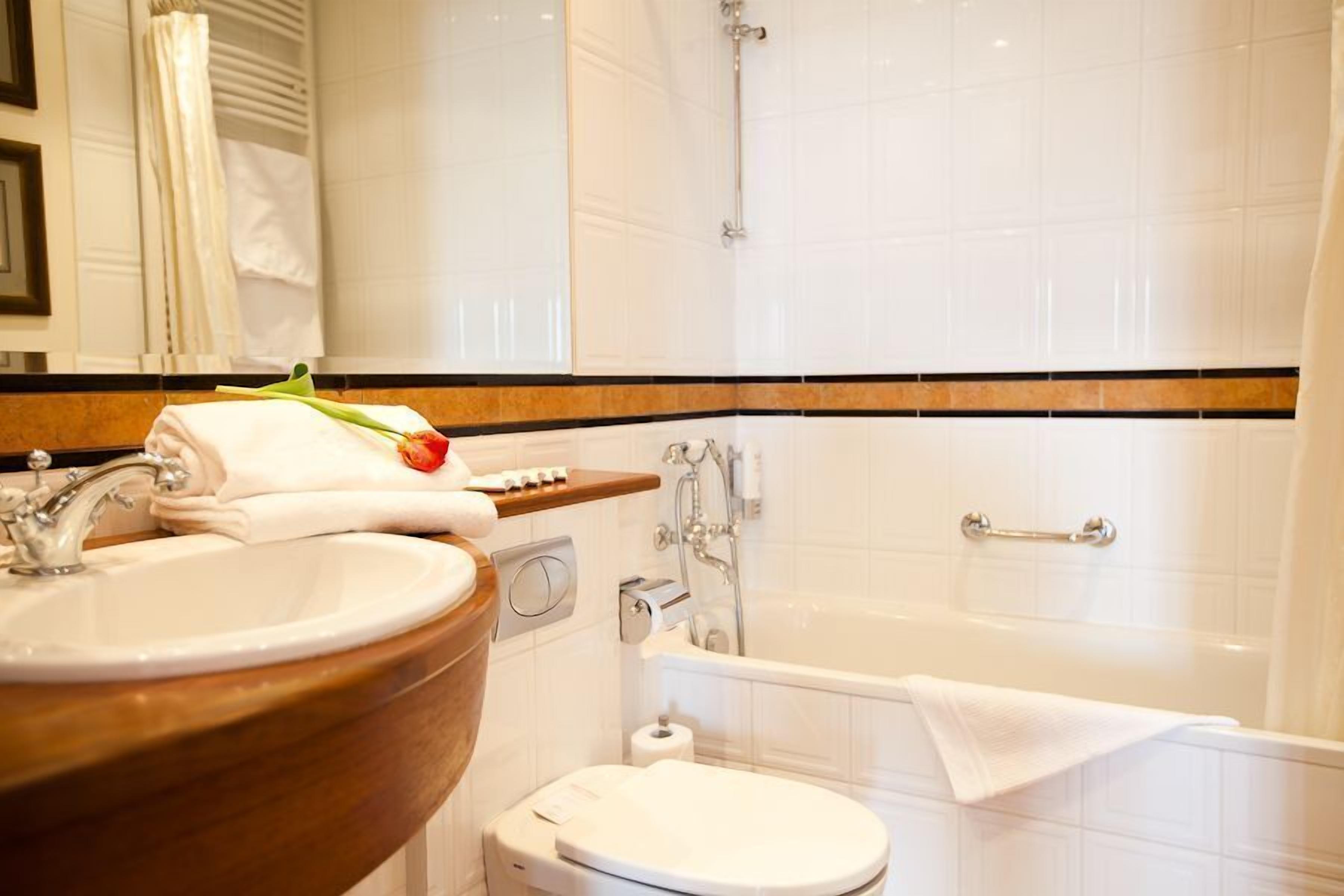 Un baño con un tocador de madera, un lavabo blanco, un inodoro y una bañera.