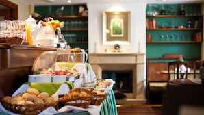 Una mesa de buffet con diversos alimentos y bebidas, una chimenea al fondo y una estantería con libros y objetos decorativos.