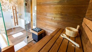 Un cuarto de sauna con paredes de madera, cabina de ducha de vidrio, banca de madera y balde de madera.