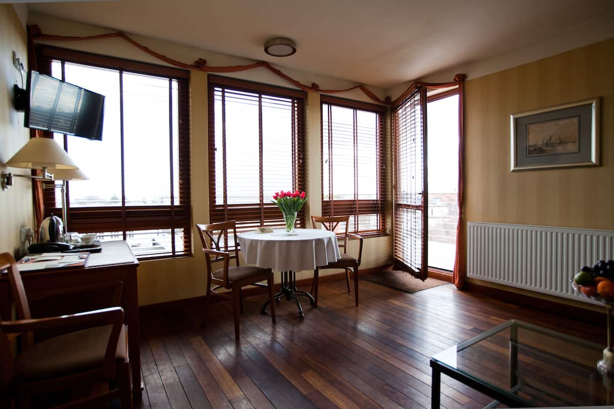 Un comedor con una mesa redonda, sillas, un florero con flores, un televisor en la pared y una ventana con persianas.