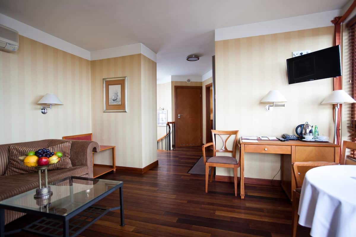 Habitación de hotel con sofá, mesa de centro de vidrio, escritorio con silla, televisor y mesa de comedor con una silla.