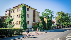 Un hotel con una columna central cubierta de follaje, un carril bici y un cielo azul despejado.