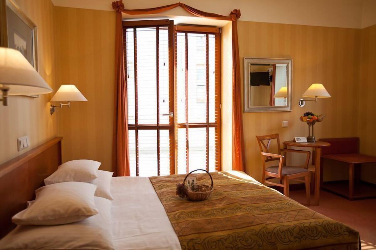 Habitación de hotel con cama, dos sillones, una mesita, un espejo y ventana con cortinas.