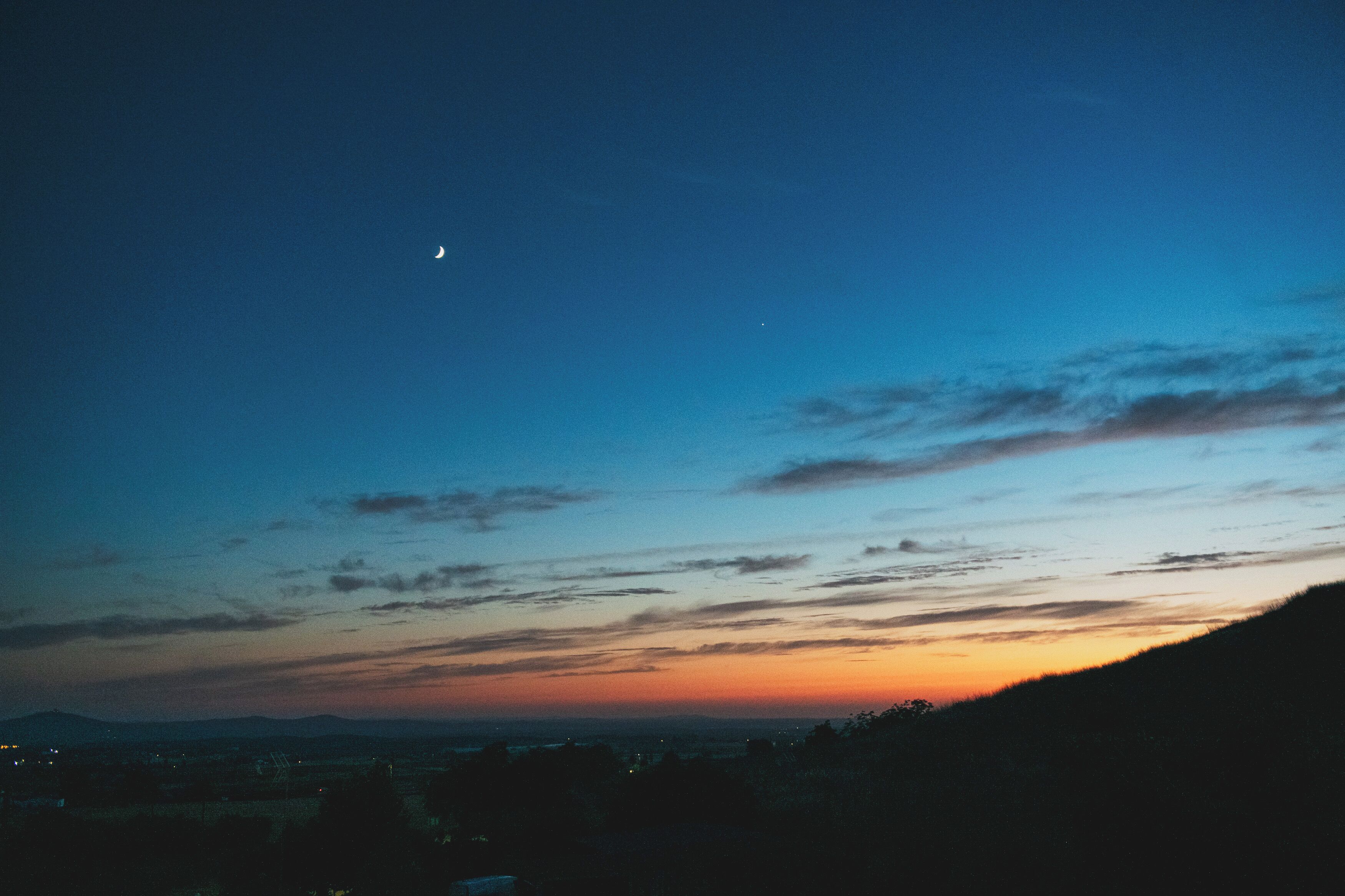 Ein Nachthimmel mit sichelförmigem Mond und vereinzelten Wolken.