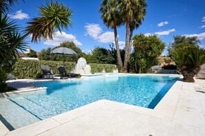 A rectangular swimming pool with clear blue water, surrounded by palm trees and a white umbrella. - Pateo dos Solares Charm Hotel (Estremoz)