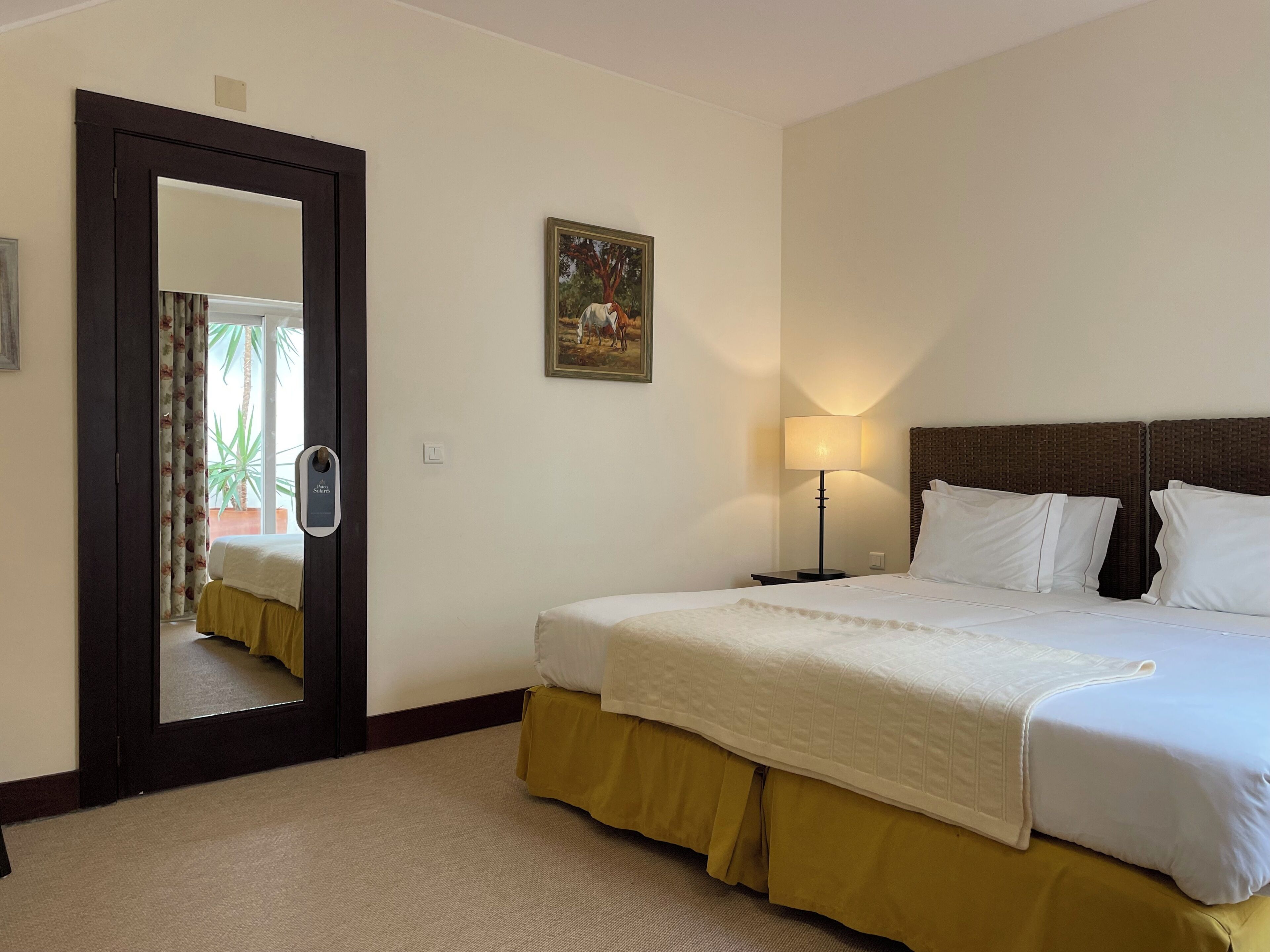 Habitación de hotel con cama, mesita de noche, lámpara, un cuadro y puerta que da a un balcón.