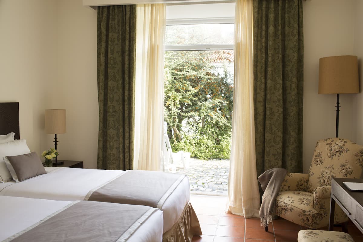 A hotel room with two beds, a chair, a desk, and a lamp.