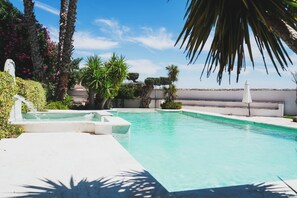 Una piscina con agua azul cristalina, rodeada de palmeras y otra vegetación.