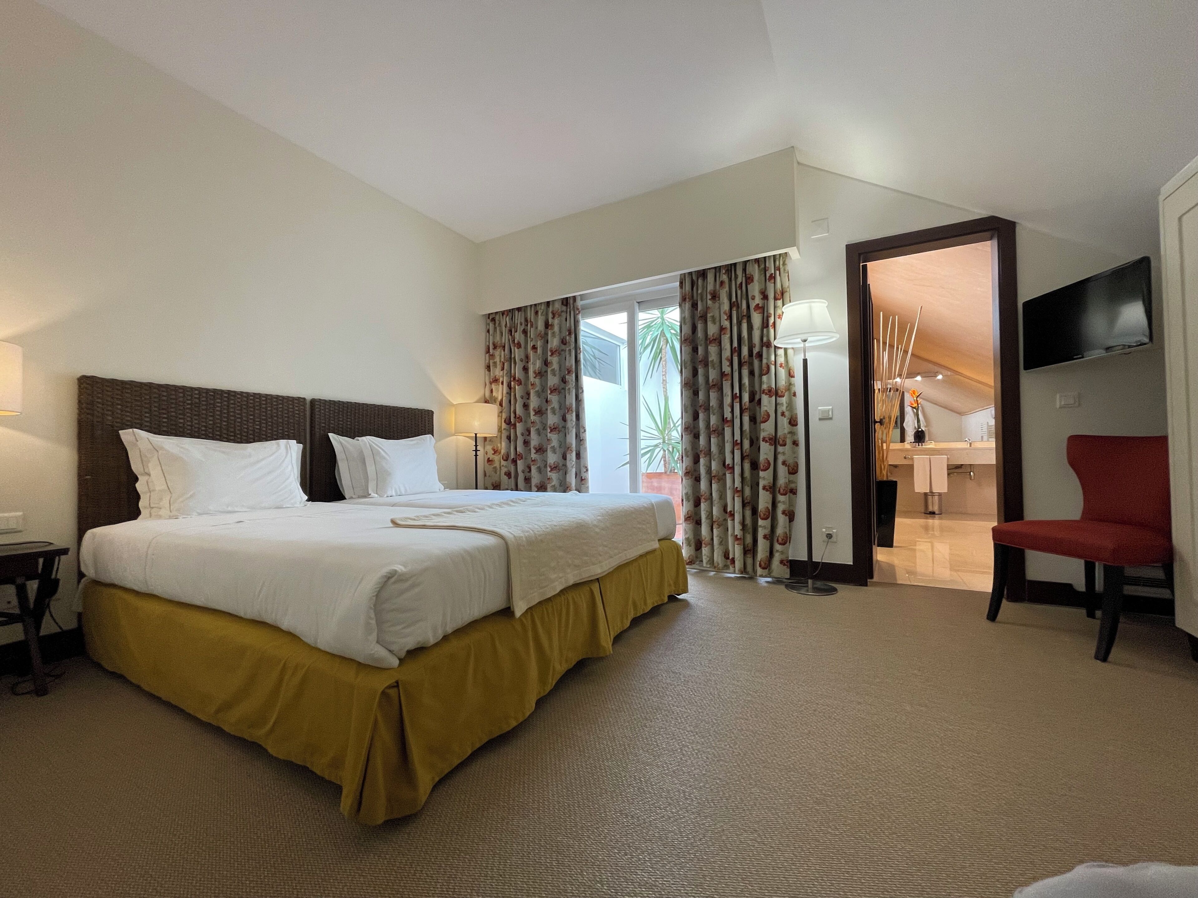 A hotel room with a large bed, a desk, a chair, a TV, and a bathroom visible through an open door.