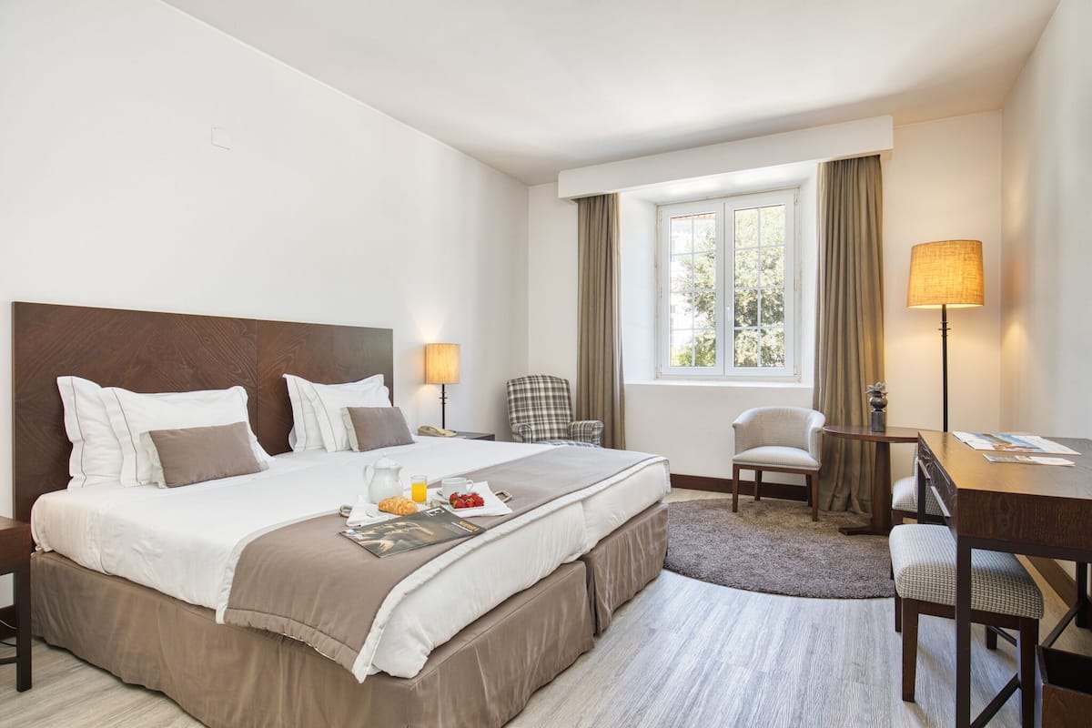 A hotel room with a large bed, a desk, a chair, and a window with curtains.