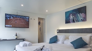 A hotel room with a bed, a TV displaying a tennis match, a painting, and a bottle of wine on a side table. - Flaminio Village Bungalow Park - Campground (Rome)