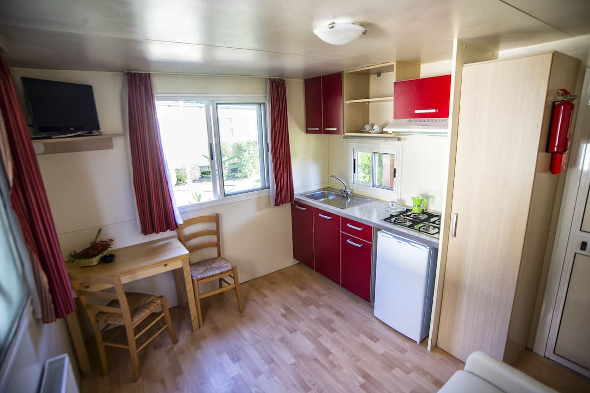 A compact kitchen with a wooden table, red cabinets, a white refrigerator, and a gas stove.