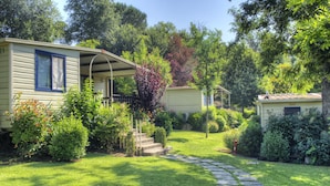 A mobile home with a porch and steps leading to a covered area, surrounded by lush greenery and a stone pathway. - Flaminio Village Bungalow Park - Campground (Rome)