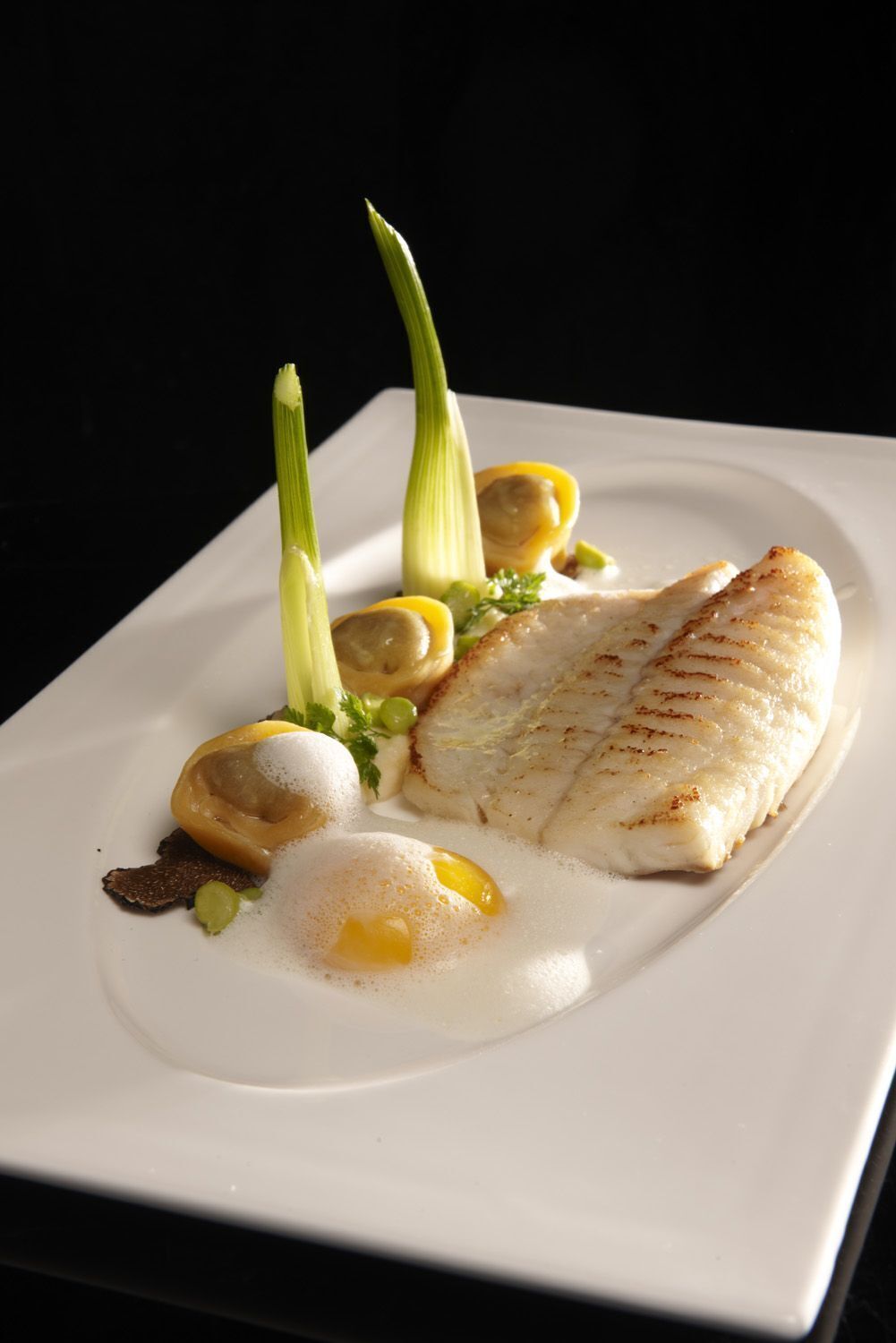 Un plato blanco con un trozo de pescado, rodajas de limón y una guarnición de hierbas verdes.