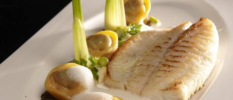 Un plato blanco con un trozo de pescado, rodajas de limón y una guarnición de hierbas verdes.