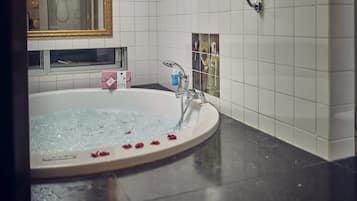 A bathtub with rose petals, a bottle of shampoo, and a framed picture on the wall.