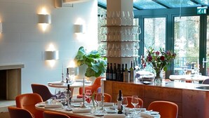 A modern restaurant interior with round tables, orange chairs, and a wine rack. - Landgoed Hotel Groot Warnsborn (Arnhem)