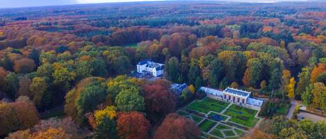 An aerial view of a large estate with a main building surrounded by expansive gardens and dense forest.