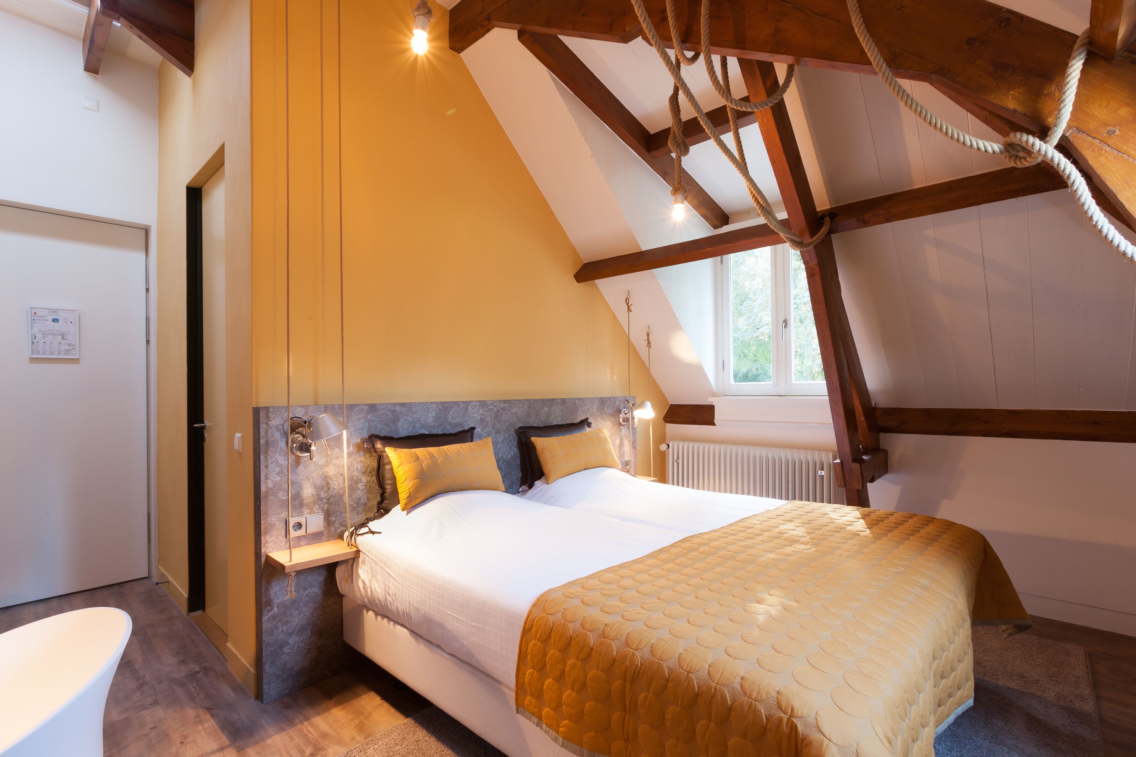 Une chambre avec un grand lit, des poutres en bois, une fenêtre et un radiateur.