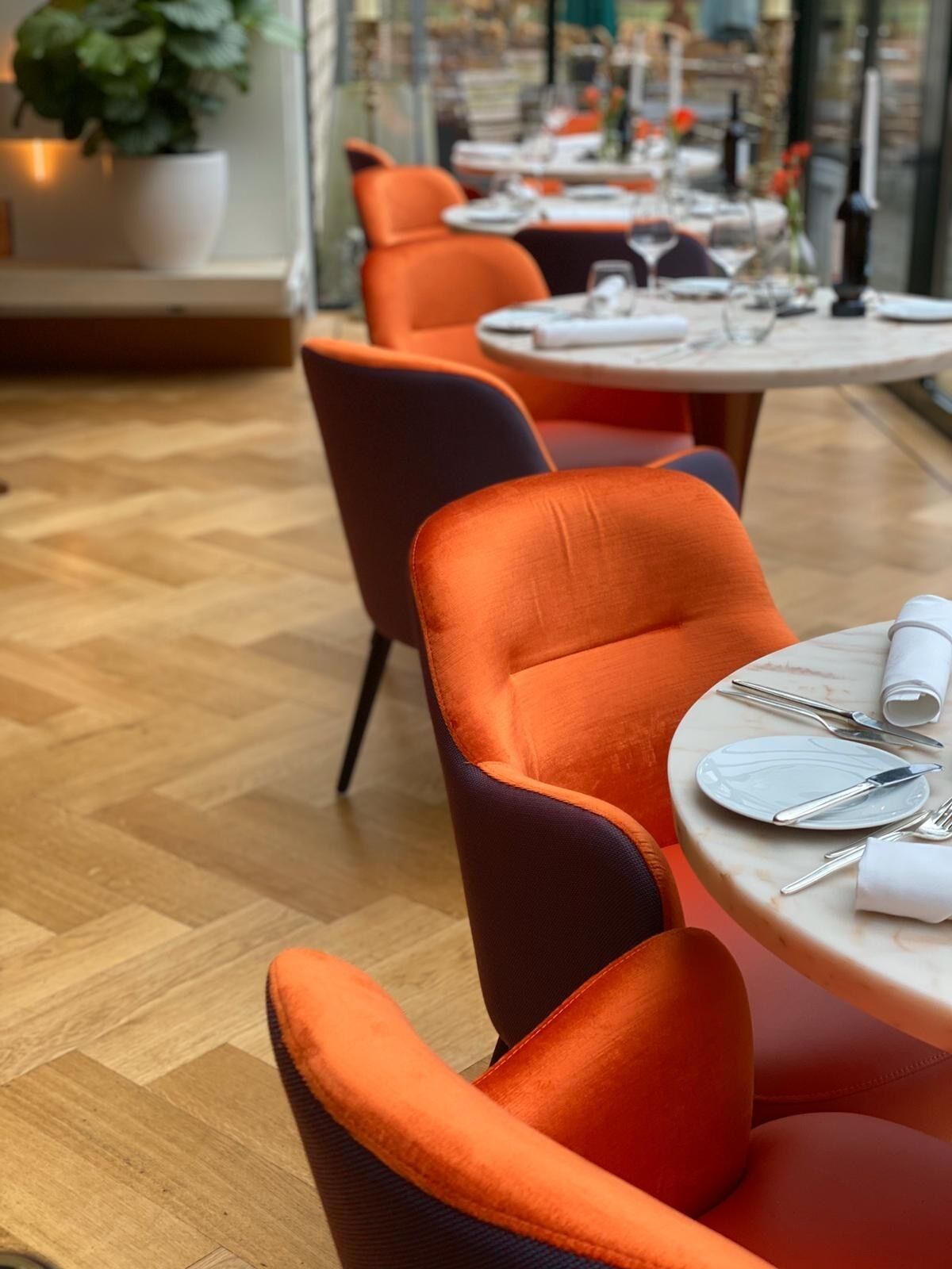 A dining area with orange upholstered chairs and a round table set for two.
