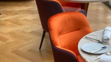 A dining area with orange upholstered chairs and a round table set for two.