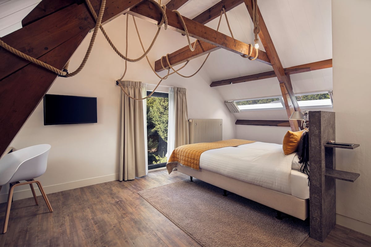 A bedroom with a sloped ceiling, a bed, a chair, and a TV.