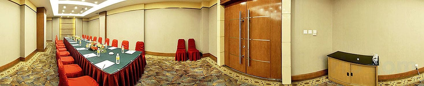 Una sala conferenze con un lungo tavolo, sedie rosse, un podio e una moquette a motivi.