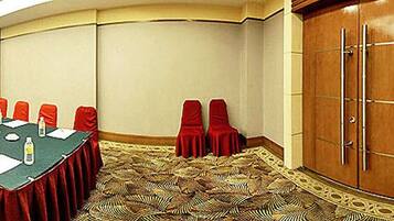 Una sala conferenze con un lungo tavolo, sedie rosse, un podio e una moquette a motivi.