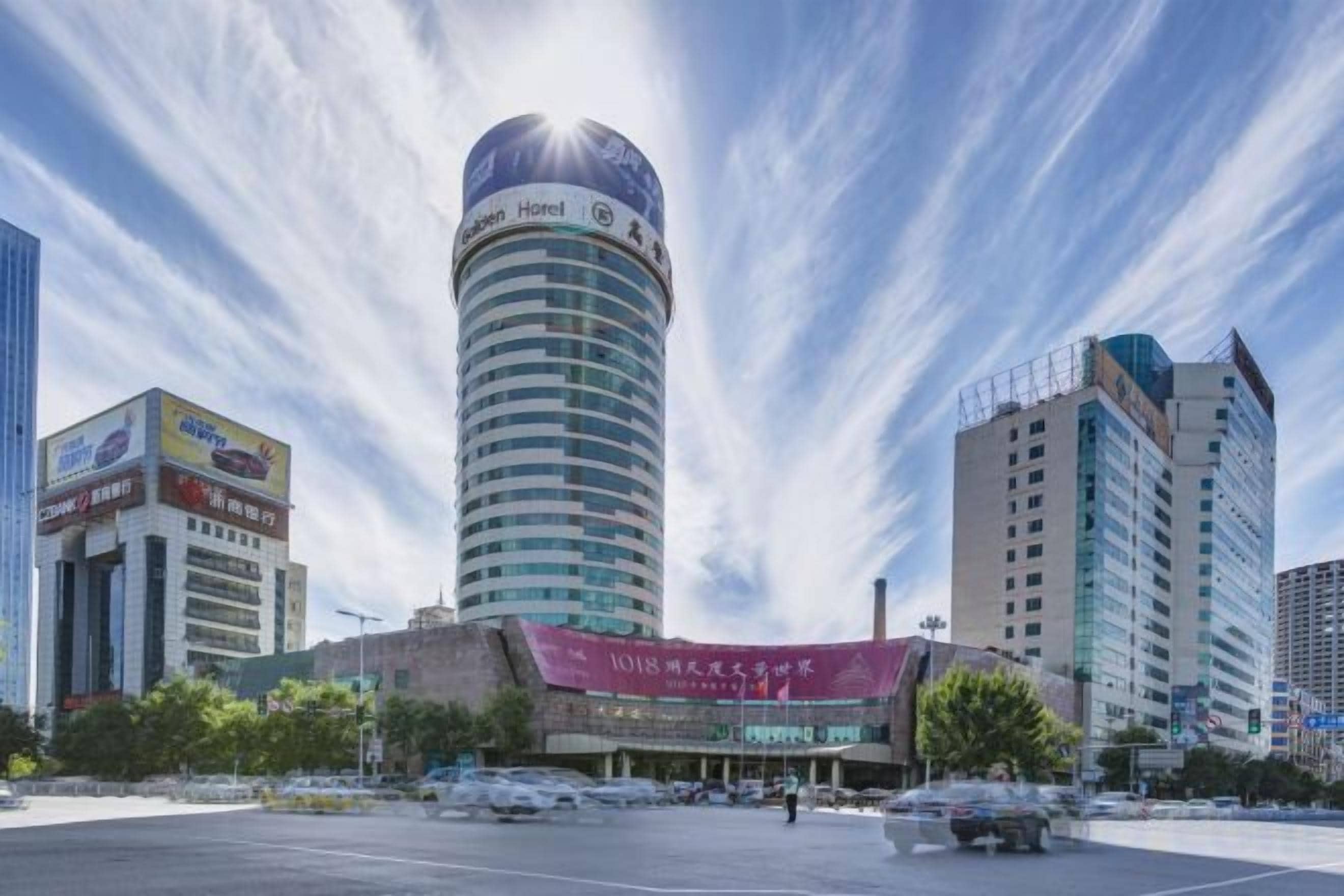 Um hotel com uma torre cilíndrica, rodeado por edifícios modernos, e um céu claro.