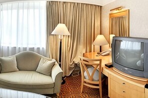 A hotel room with a sofa, a desk with a lamp, a television, and a large window with curtains. - Golden Hotel (Shenyang)