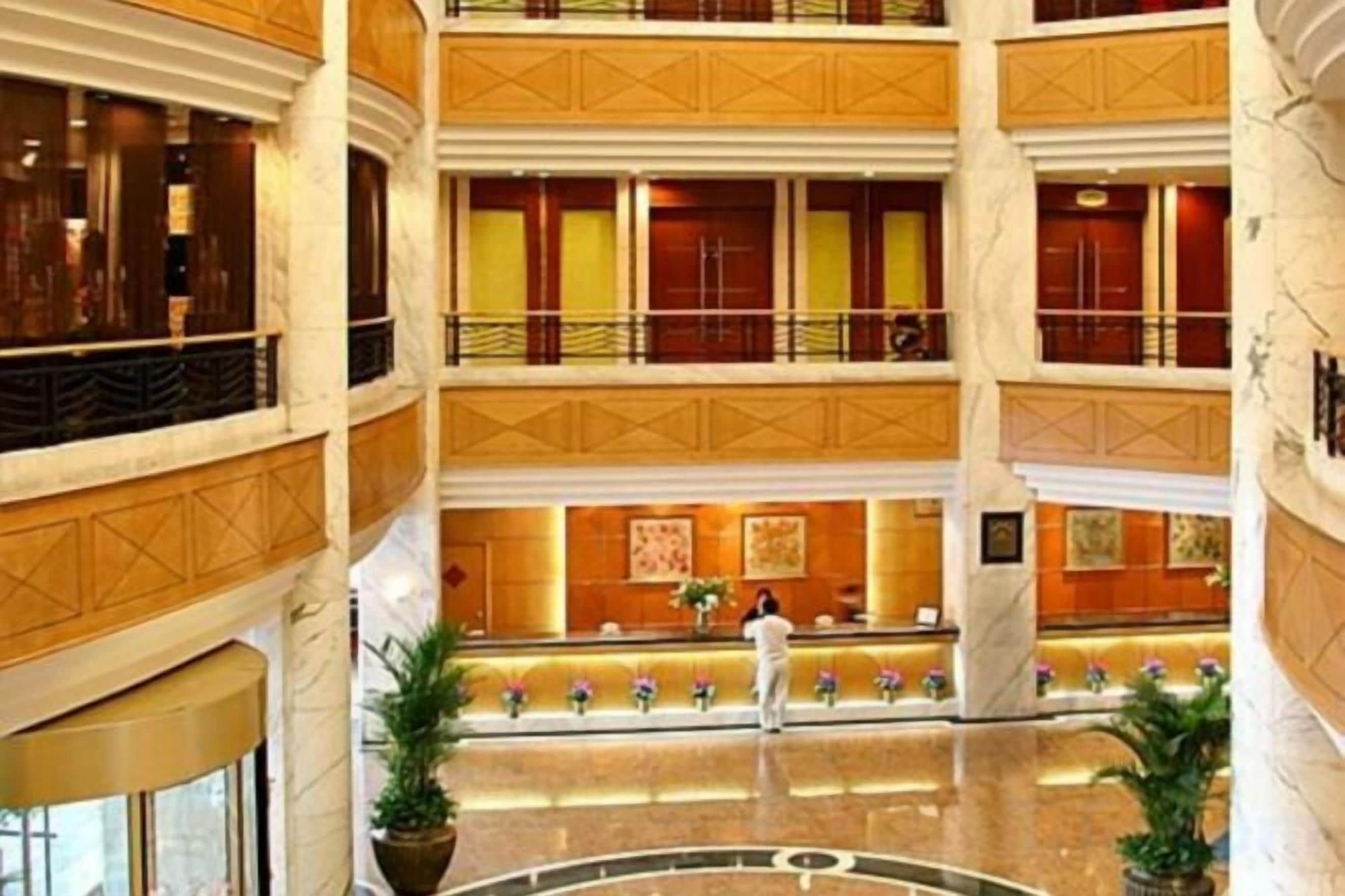 Vestíbulo de hotel de varios niveles con un atrio central, una mesa de recepción y una persona de pie cerca de la mesa.
