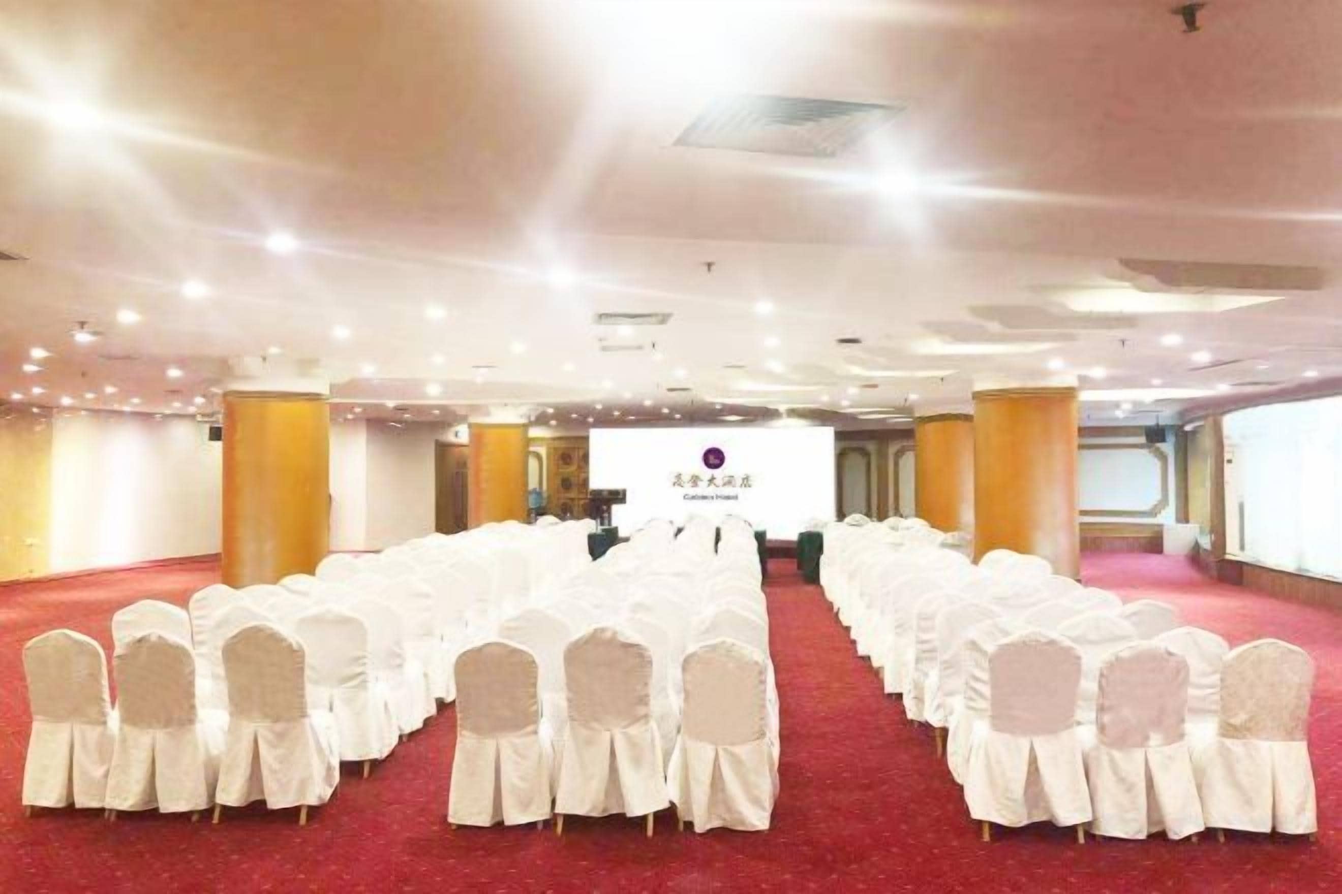 A conference room with rows of white chairs, a stage with a podium, and a red carpet.
