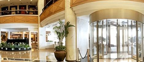 Un vestíbulo de hotel con un atrio central, una recepción y una gran planta en maceta.