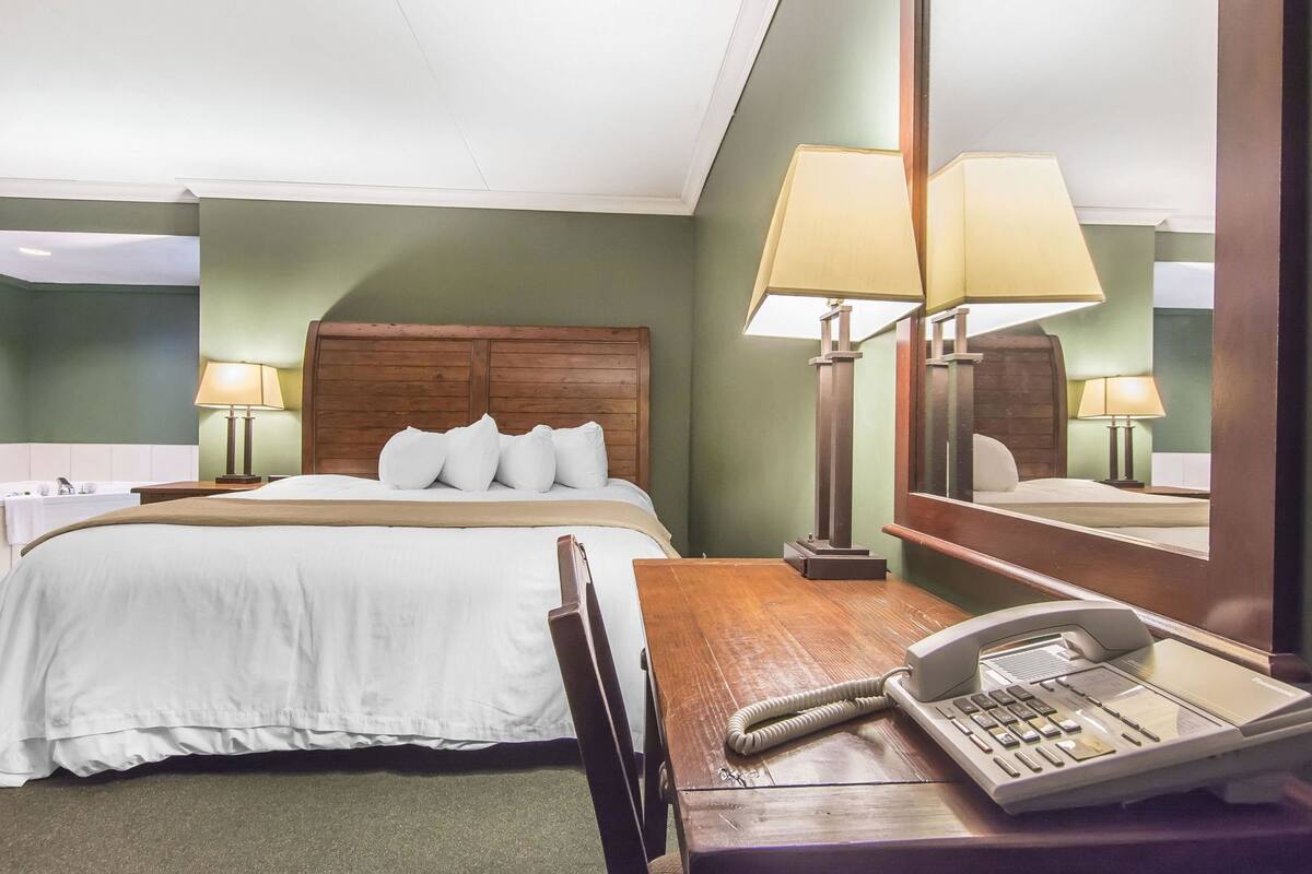 Una habitación de hotel con una cama, lámparas de noche, un escritorio con teléfono y un espejo.