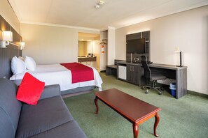 A hotel room with a bed, a desk, a chair, a sofa, and a small table. - Rodeway Inn King William (Huntsville)