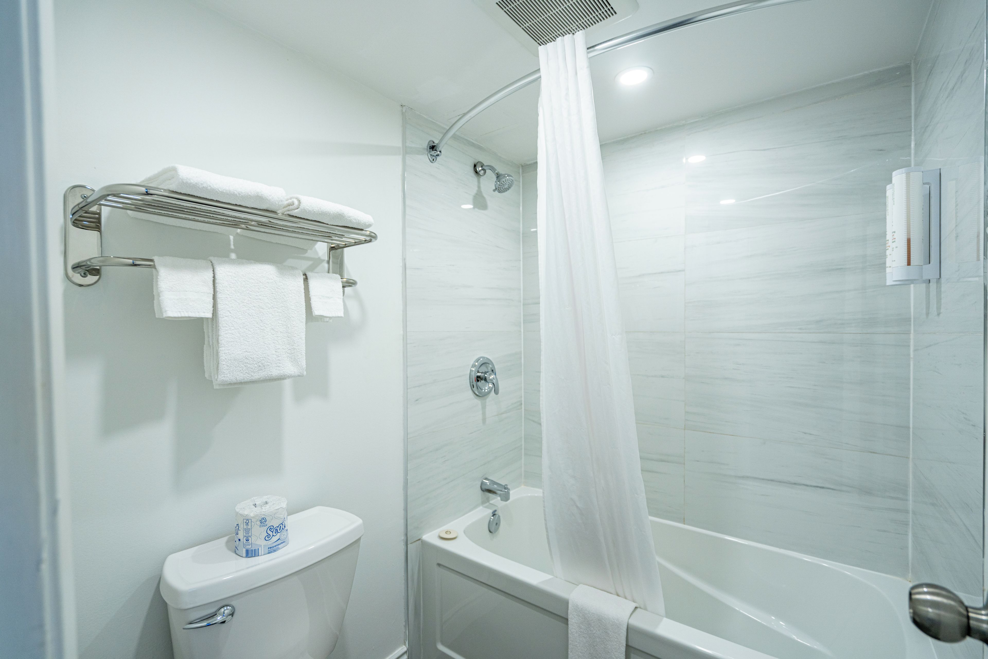 A bathroom with a shower, toilet, and a towel rack with towels.